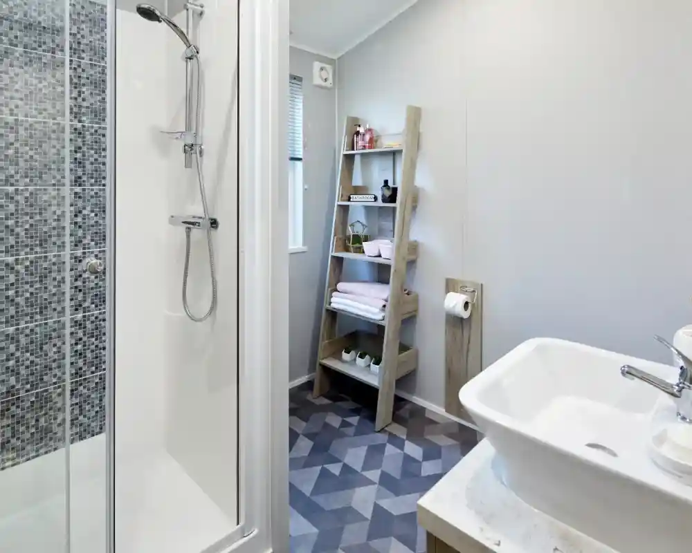 Modern bathroom featuring a tiled shower, white vessel sink, and a wooden ladder shelf with toiletries and towels.