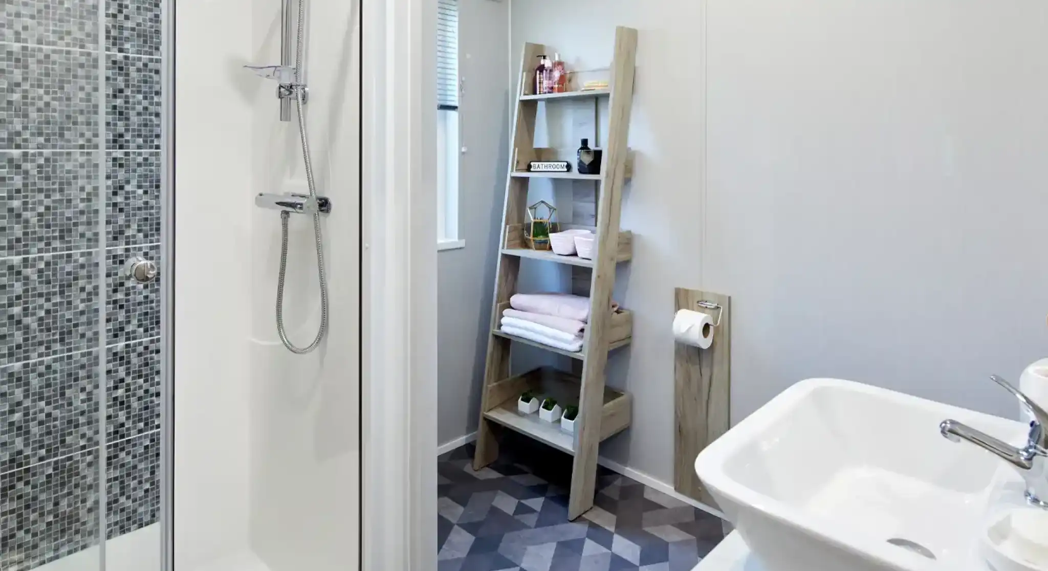 Modern bathroom featuring a tiled shower, white vessel sink, and a wooden ladder shelf with toiletries and towels.