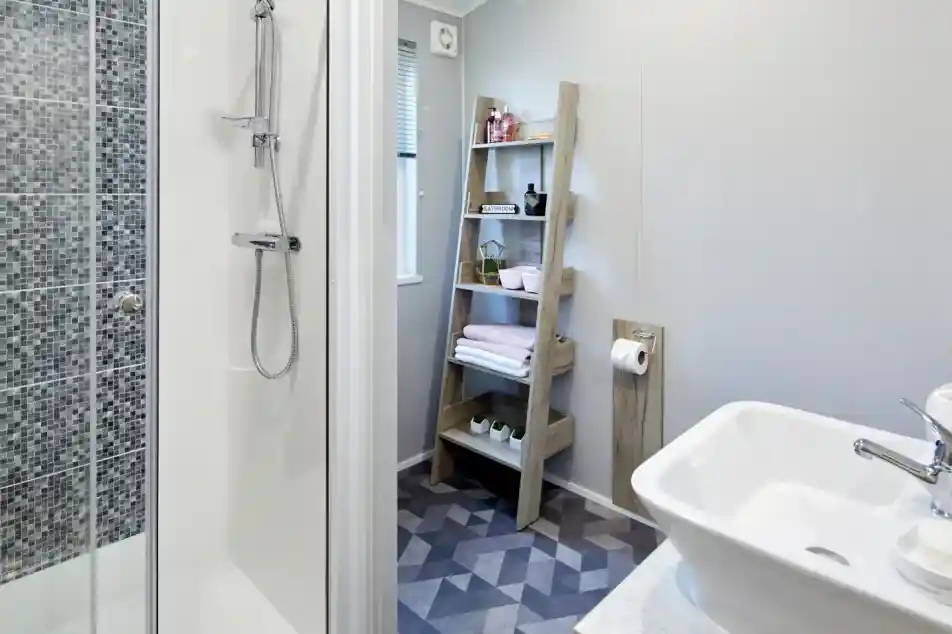 Modern bathroom featuring a tiled shower, white vessel sink, and a wooden ladder shelf with toiletries and towels.