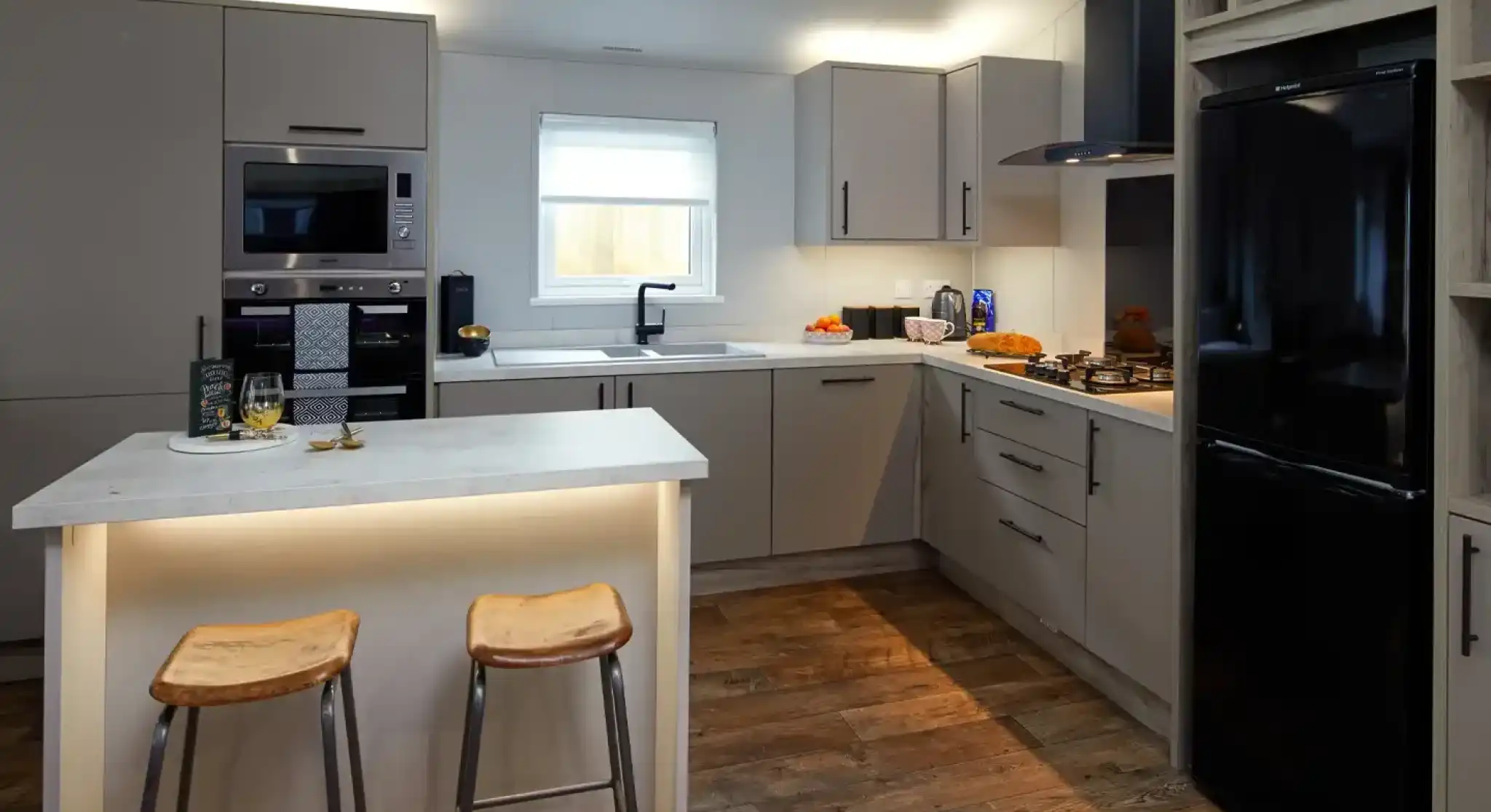 Modern kitchen with grey cabinets, stainless steel appliances, a black refrigerator, and a central island with two stools.