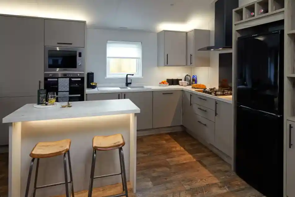 Modern kitchen with grey cabinets, stainless steel appliances, a black refrigerator, and a central island with two stools.
