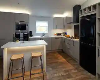 Modern kitchen with grey cabinets, stainless steel appliances, a black refrigerator, and a central island with two stools.