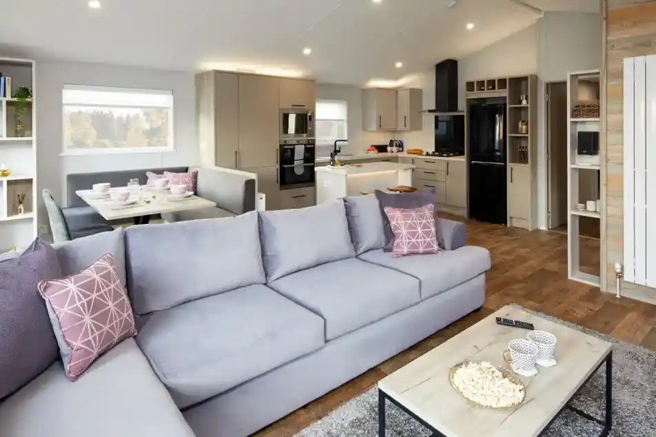 Modern living room with light grey sectional sofa facing a coffee table with popcorn and a modern kitchen with island and dining nook in the background.