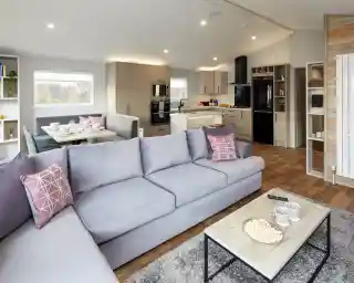 Modern living room with light grey sectional sofa facing a coffee table with popcorn and a modern kitchen with island and dining nook in the background.