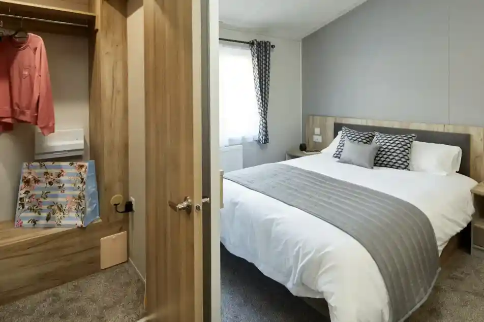 View into a bedroom with a made bed and an adjacent closet with clothing and a floral bag.