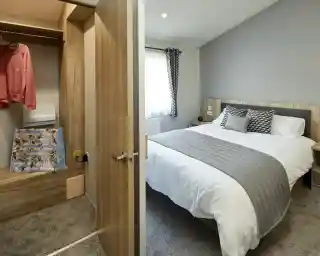 View into a bedroom with a made bed and an adjacent closet with clothing and a floral bag.