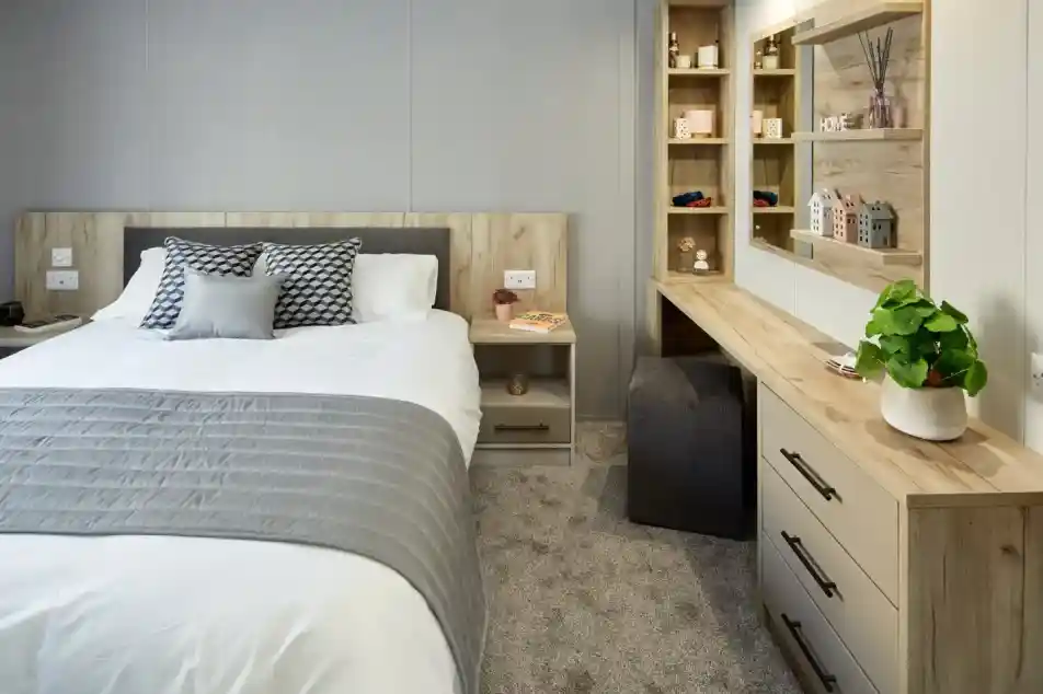 A modern bedroom with a neatly made bed, a vanity with a mirror, and a bedside table.