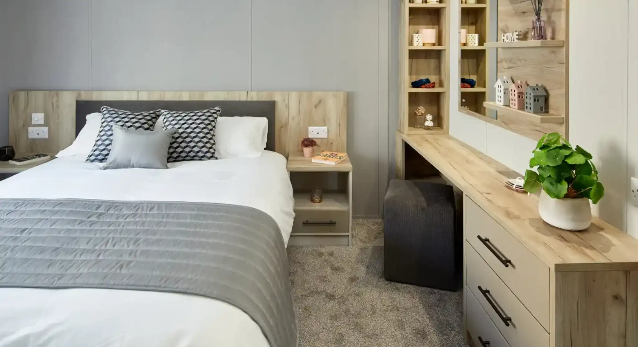 A modern bedroom with a neatly made bed, a vanity with a mirror, and a bedside table.