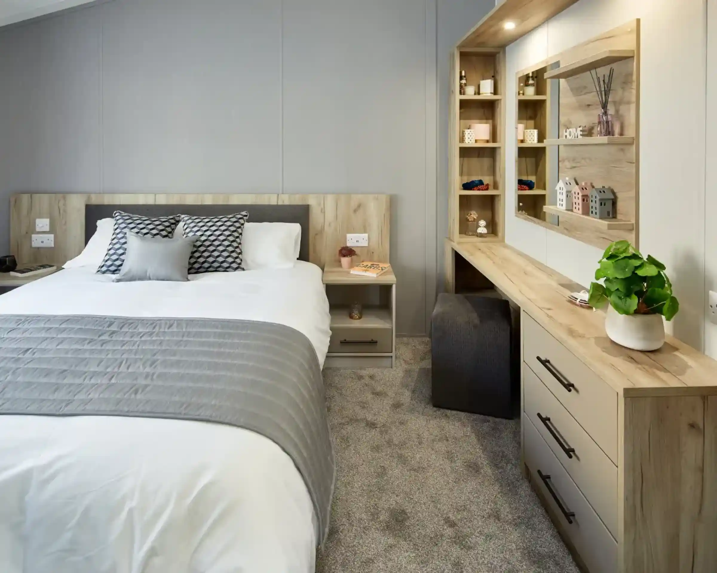 A modern bedroom with a neatly made bed, a vanity with a mirror, and a bedside table.