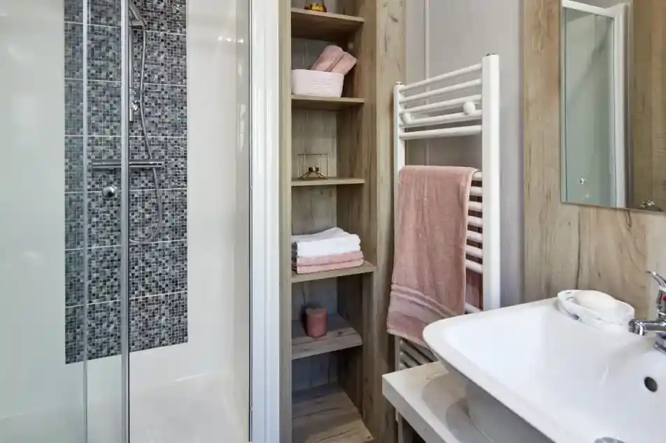 Modern bathroom with a glass-enclosed shower, open shelving, and a white sink with a towel rack.