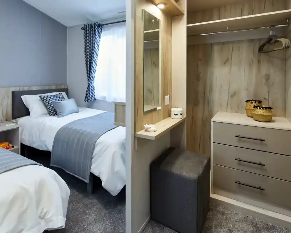 A bedroom with two beds, a closet with a vanity and stool, and a window with patterned curtains.