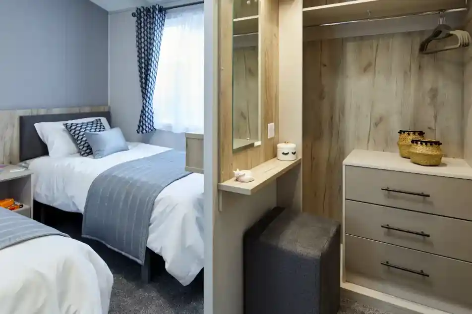 A bedroom with two beds, a closet with a vanity and stool, and a window with patterned curtains.