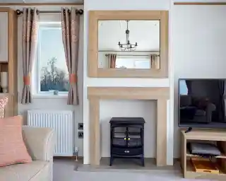 Stylish lounge area in the ABI Ambleside holiday home, featuring a wood-framed mirror above a modern fireplace with an electric log-effect stove, flanked by a window with patterned curtains and a flat-screen TV on a wooden media unit.