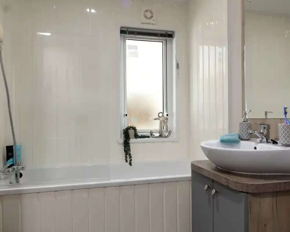Modern bathroom with a white tub and frosted window. A leafy plant hangs by the window. Sleek sink on a wooden vanity, giving a clean, tranquil feel.