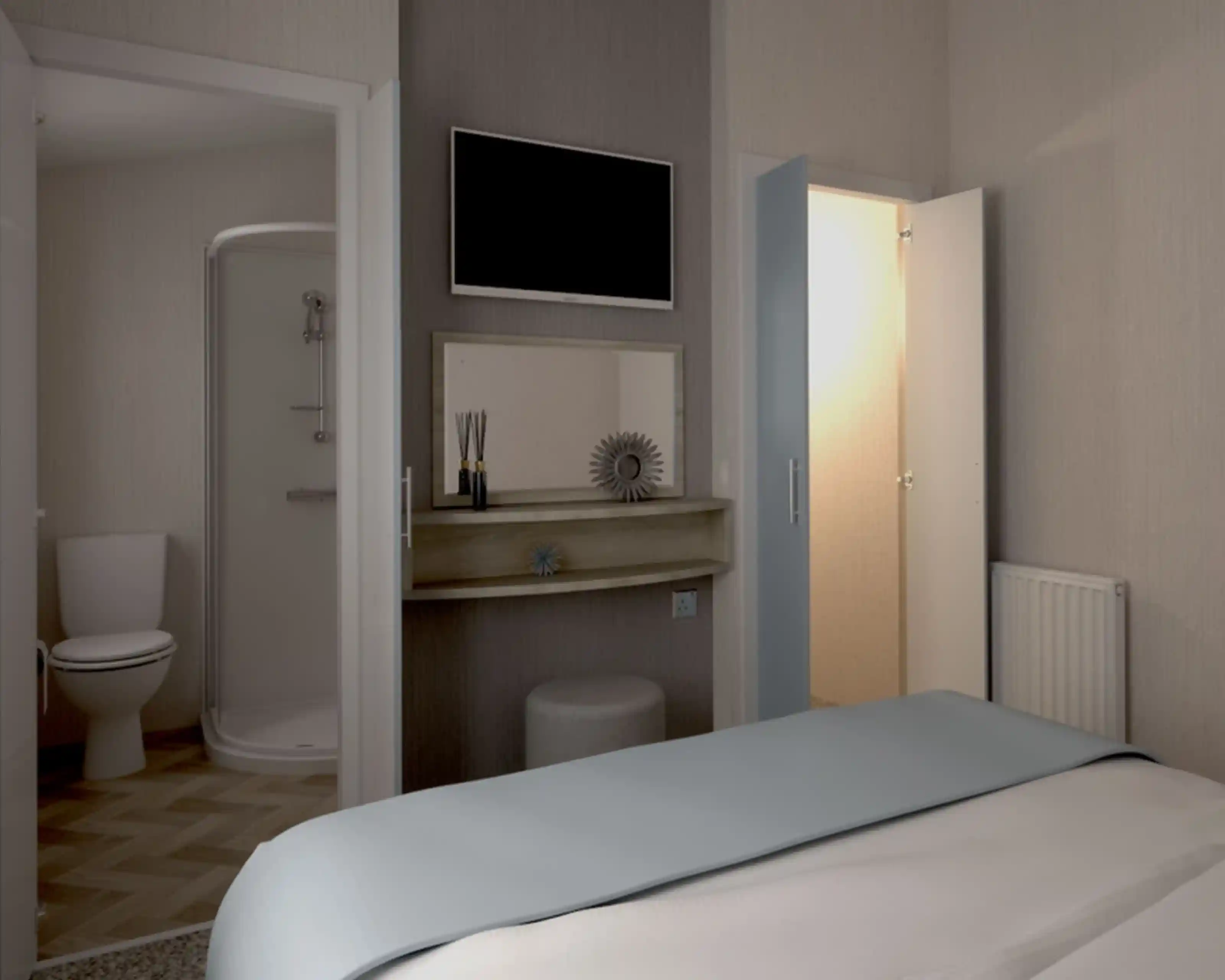 Cozy bedroom with a light blue bedspread, featuring a mounted TV on the wall. A shelf with decorative items sits near a door leading to an ensuite bathroom with a shower and toilet. A second door leads to a small wardrobe, and a radiator is visible on the wall.