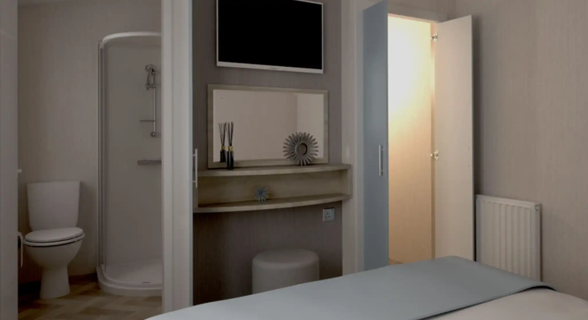 Cozy bedroom with a light blue bedspread, featuring a mounted TV on the wall. A shelf with decorative items sits near a door leading to an ensuite bathroom with a shower and toilet. A second door leads to a small wardrobe, and a radiator is visible on the wall.