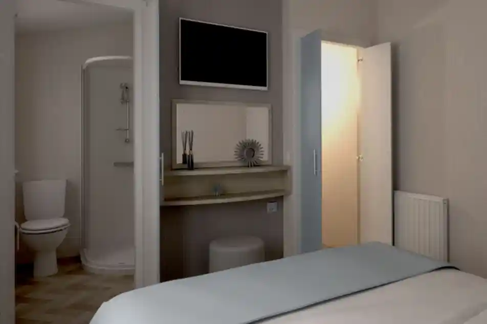 Cozy bedroom with a light blue bedspread, featuring a mounted TV on the wall. A shelf with decorative items sits near a door leading to an ensuite bathroom with a shower and toilet. A second door leads to a small wardrobe, and a radiator is visible on the wall.