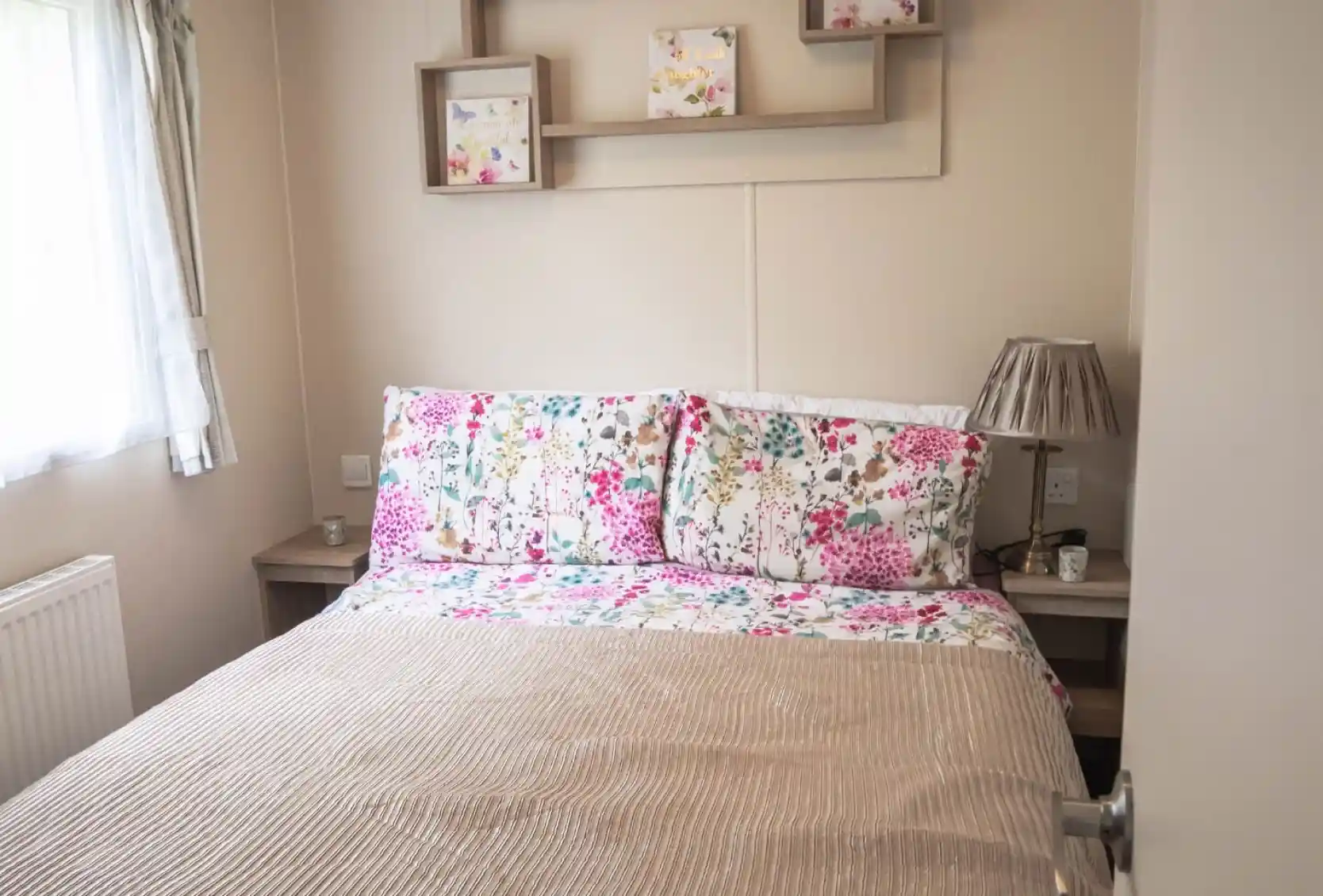 A cosy bed with a floral bedspread positioned near a window, allowing natural light to brighten the room.