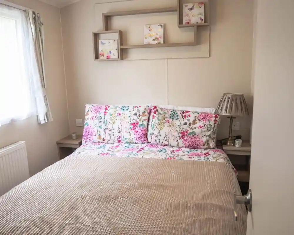 A cosy bed with a floral bedspread positioned near a window, allowing natural light to brighten the room.