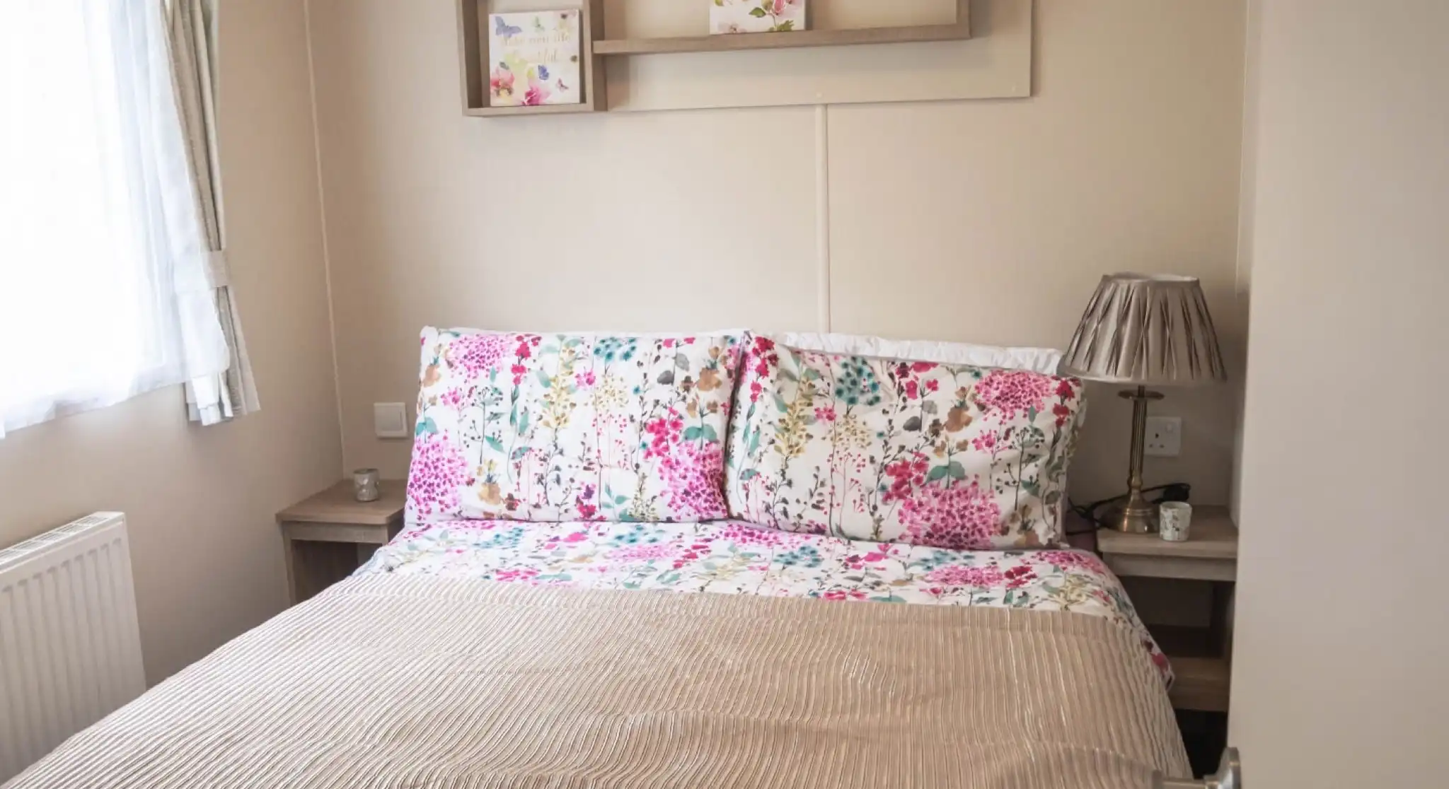 A cosy bed with a floral bedspread positioned near a window, allowing natural light to brighten the room.