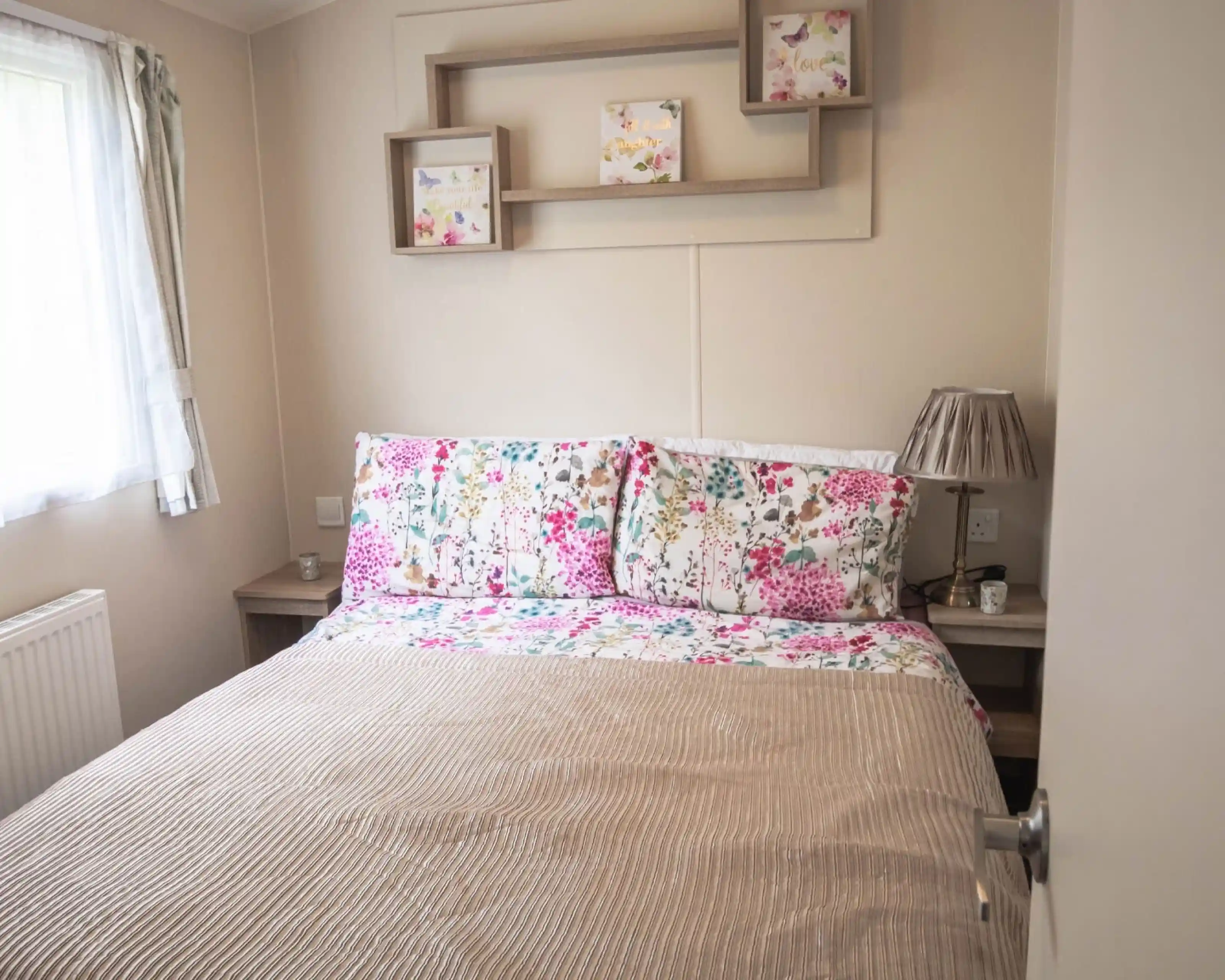 A cosy bed with a floral bedspread positioned near a window, allowing natural light to brighten the room.