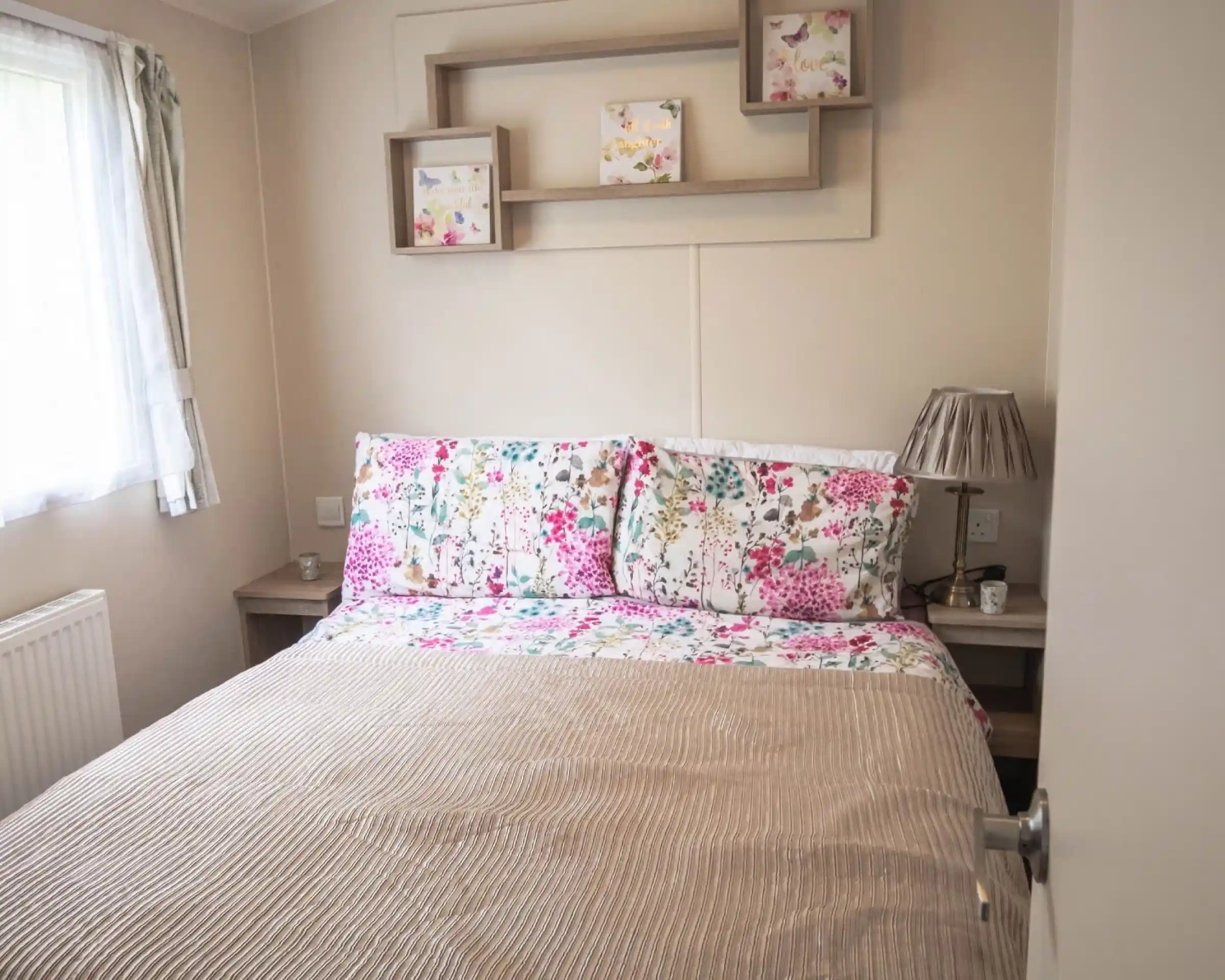 A cosy bed with a floral bedspread positioned near a window, allowing natural light to brighten the room.