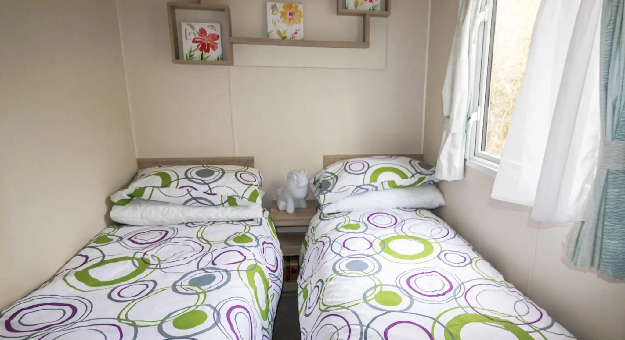 A second bedroom featuring two twin beds, neatly made with simple bedding and a window allowing natural light