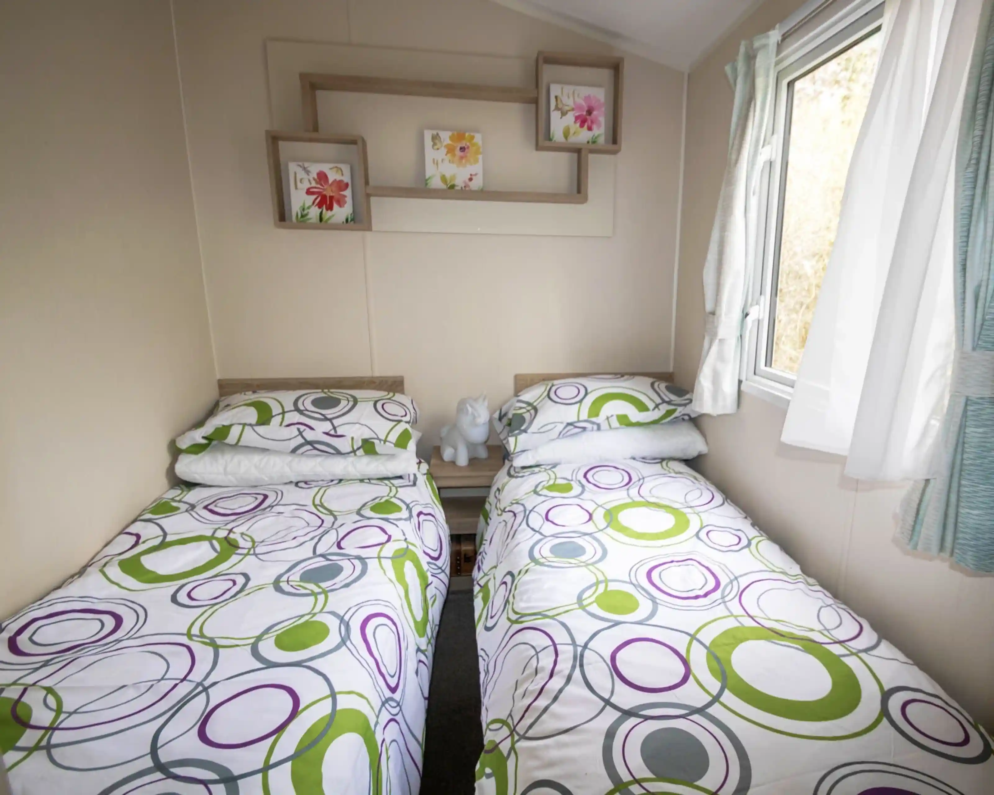 A second bedroom featuring two twin beds, neatly made with simple bedding and a window allowing natural light