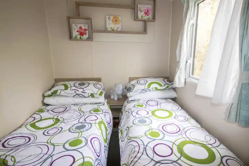 A second bedroom featuring two twin beds, neatly made with simple bedding and a window allowing natural light