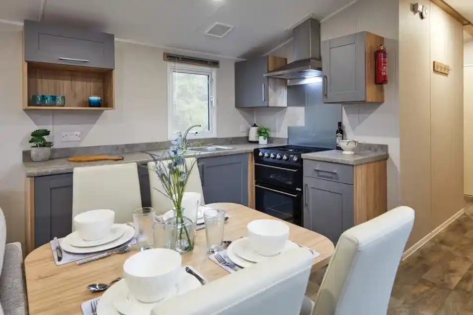 Modern kitchen and dining area in a holiday caravan with grey and wood cabinetry, set dining table, and a warm, contemporary design.