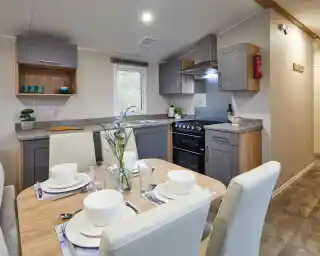 Modern kitchen and dining area in a holiday caravan with grey and wood cabinetry, set dining table, and a warm, contemporary design.
