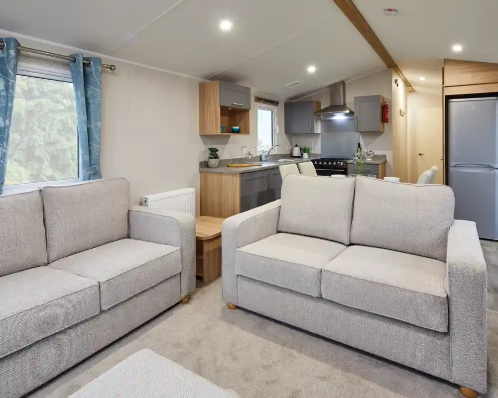 Two grey sofas in a modern living room and kitchen in the background with free-standing fridge freezer, grey cabinetry, stove and sink.