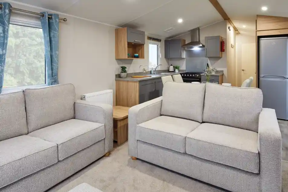 Two grey sofas in a modern living room and kitchen in the background with free-standing fridge freezer, grey cabinetry, stove and sink.