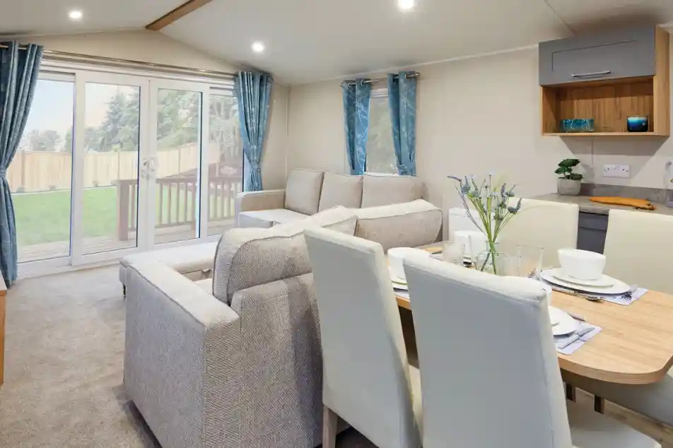 Modern living room and dining area with a two beige sofas, a dining table with cream dining chairs, and sliding glass doors leading outside.