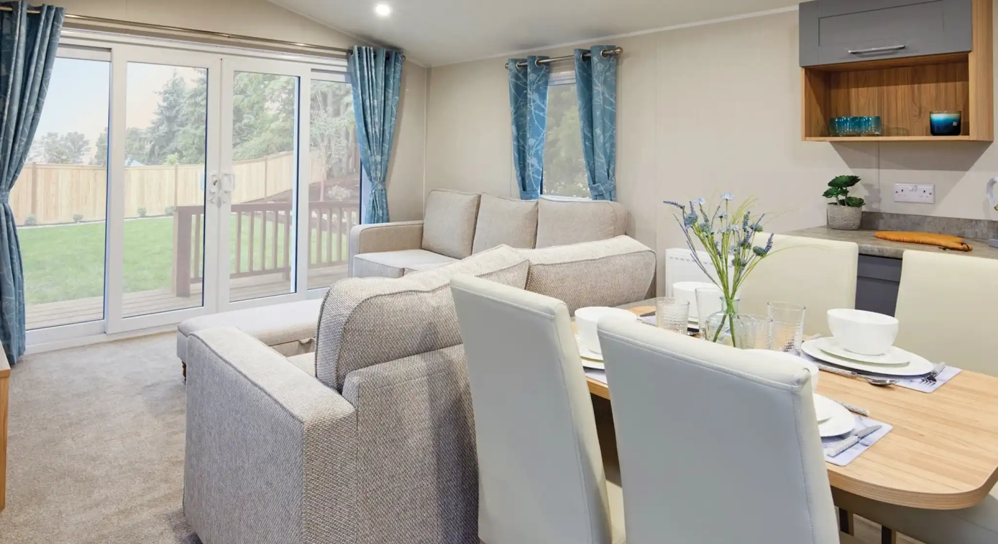 Modern living room and dining area with a two beige sofas, a dining table with cream dining chairs, and sliding glass doors leading outside.