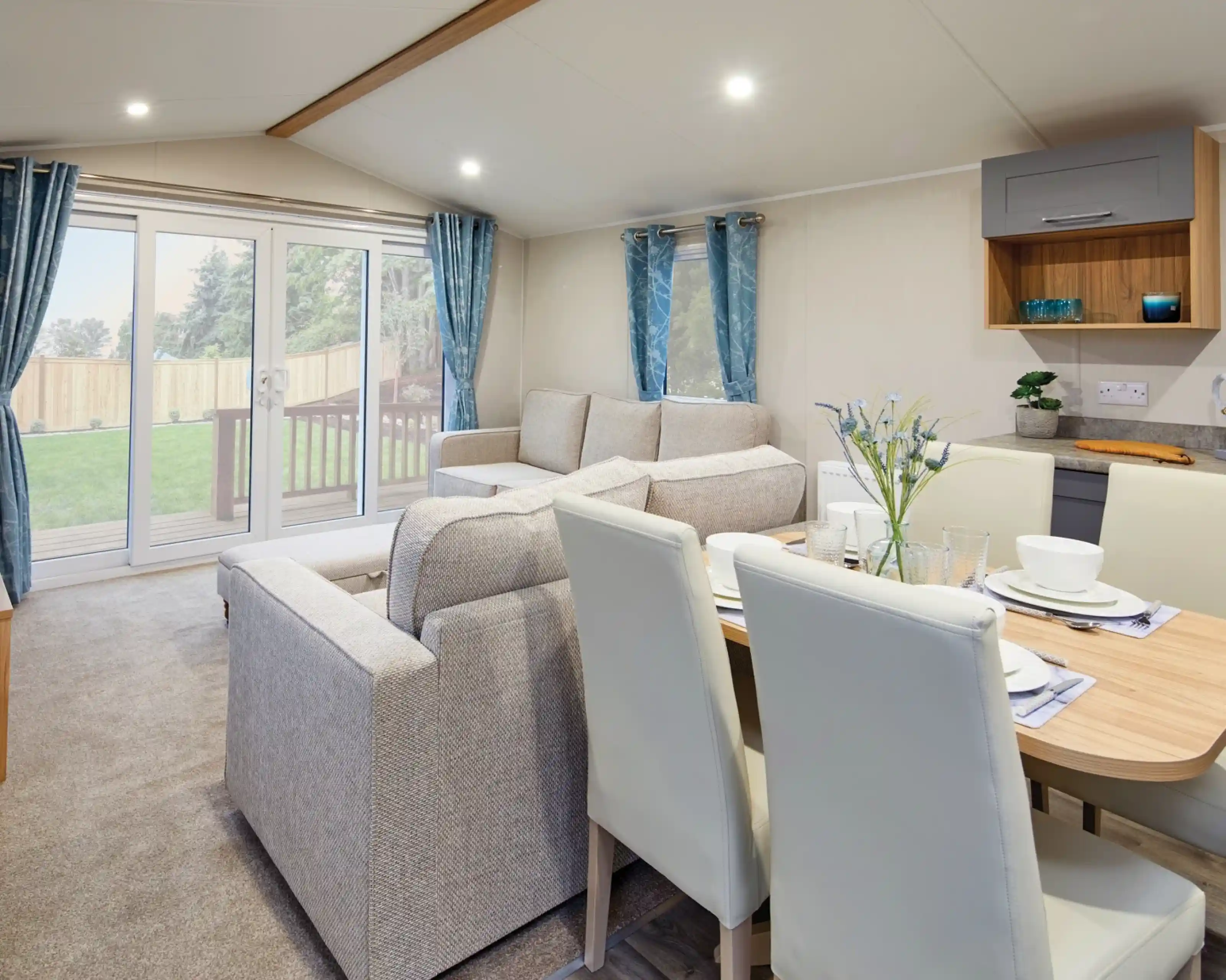 Modern living room and dining area with a two beige sofas, a dining table with cream dining chairs, and sliding glass doors leading outside.