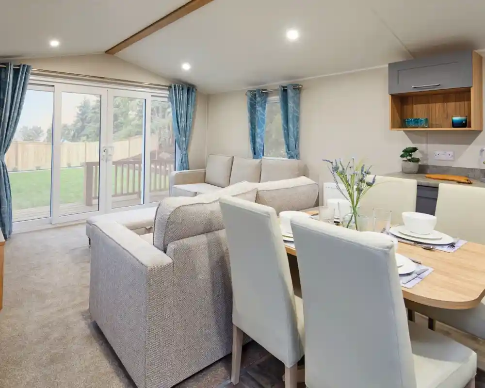 Modern living room and dining area with a two beige sofas, a dining table with cream dining chairs, and sliding glass doors leading outside.