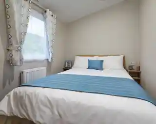 Bright master bedroom in a holiday caravan with white linens, blue accents, light wood furniture, and soft neutral décor for a calm, inviting feel.