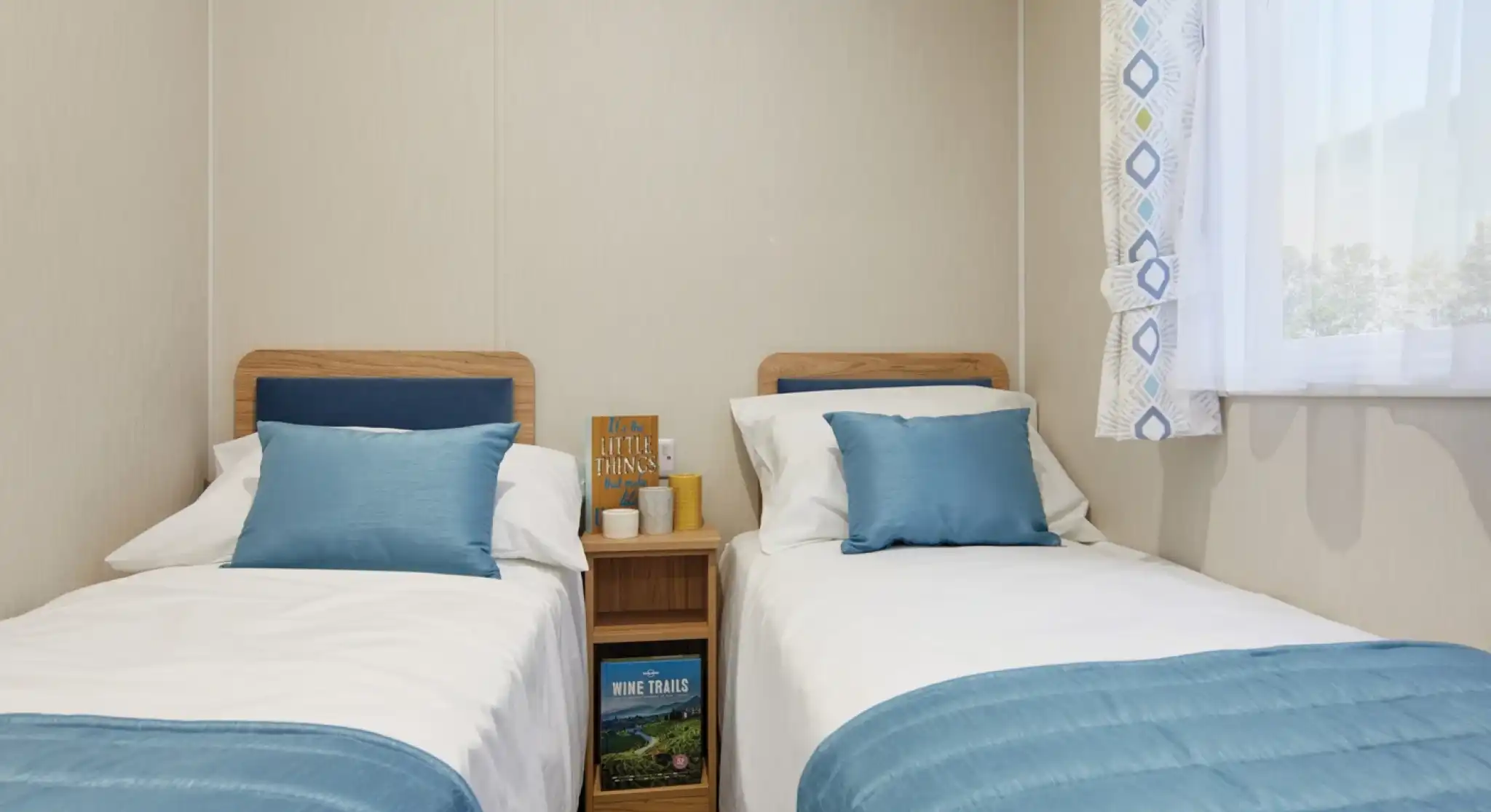 Twin bedroom in a holiday caravan with two single beds, white linens, blue accents, light wood furniture, and a bright, airy feel.