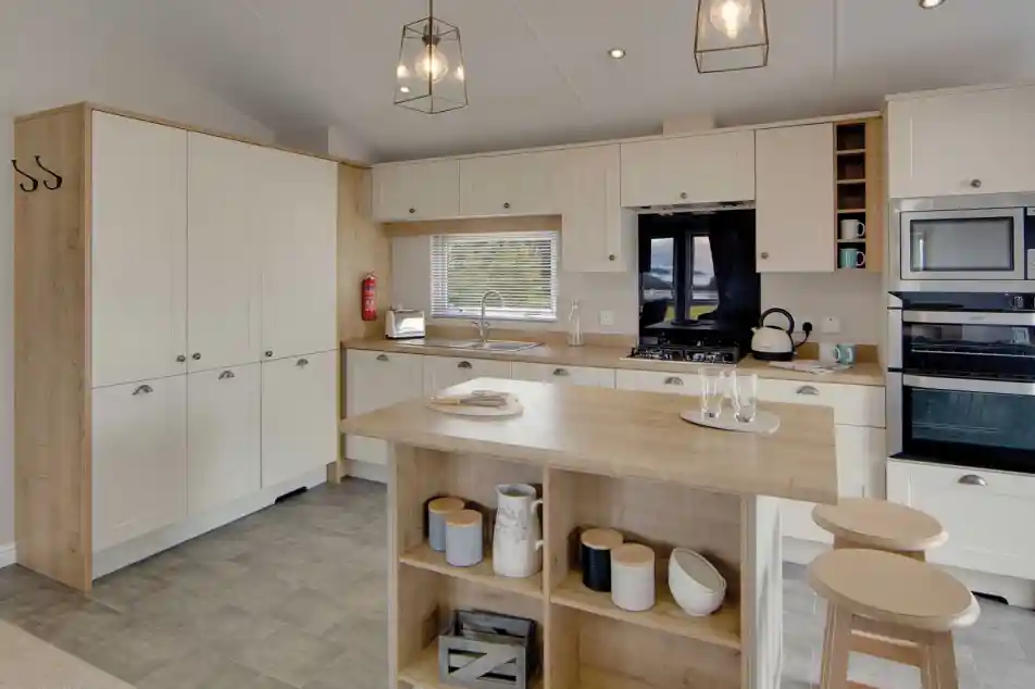Modern kitchen with cream cabinets and wood accents, featuring a central island with stools, pendant lights, and stainless steel appliances. Cozy and inviting atmosphere.