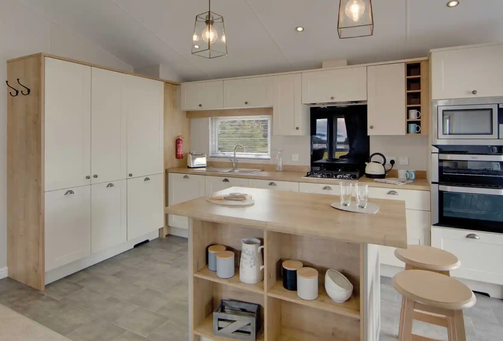 Modern kitchen with cream cabinets and wood accents, featuring a central island with stools, pendant lights, and stainless steel appliances. Cozy and inviting atmosphere.