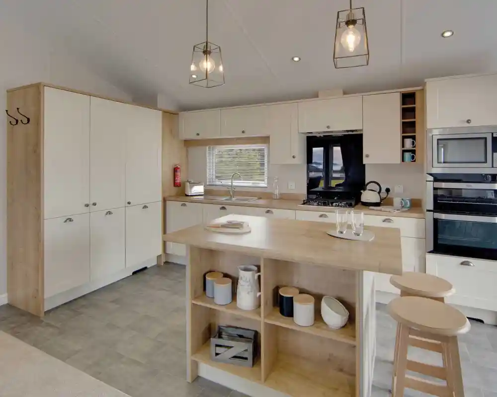 Modern kitchen with cream cabinets and wood accents, featuring a central island with stools, pendant lights, and stainless steel appliances. Cozy and inviting atmosphere.