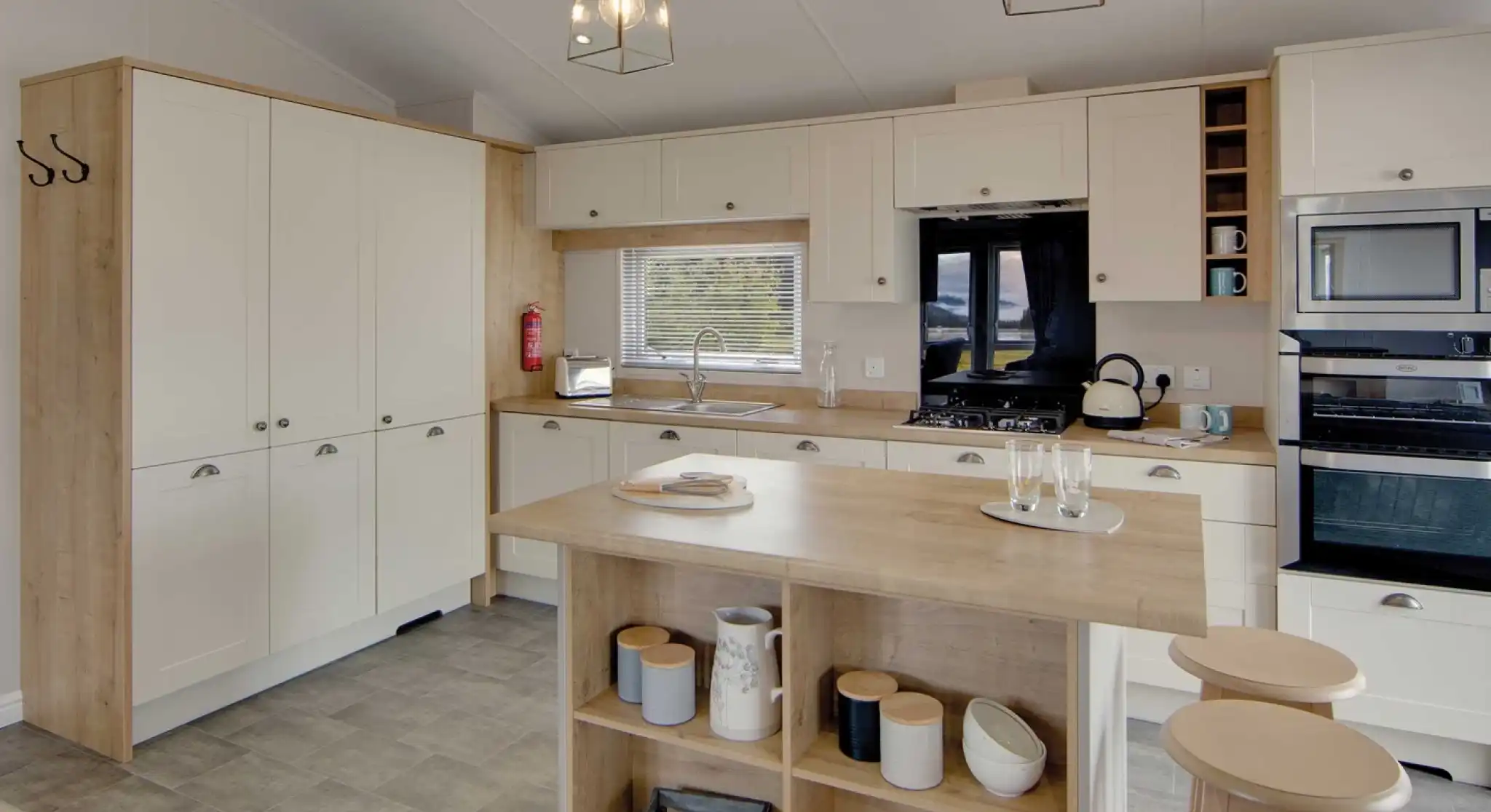 Modern kitchen with cream cabinets and wood accents, featuring a central island with stools, pendant lights, and stainless steel appliances. Cozy and inviting atmosphere.