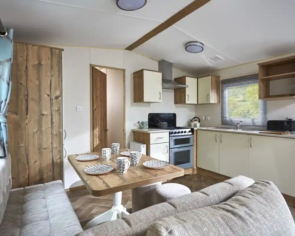 Modern mobile home kitchen and dining area with a sofa and table set for four.