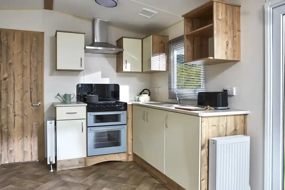 A modern caravan kitchen with cream cabinets, a double oven, and wooden accents.