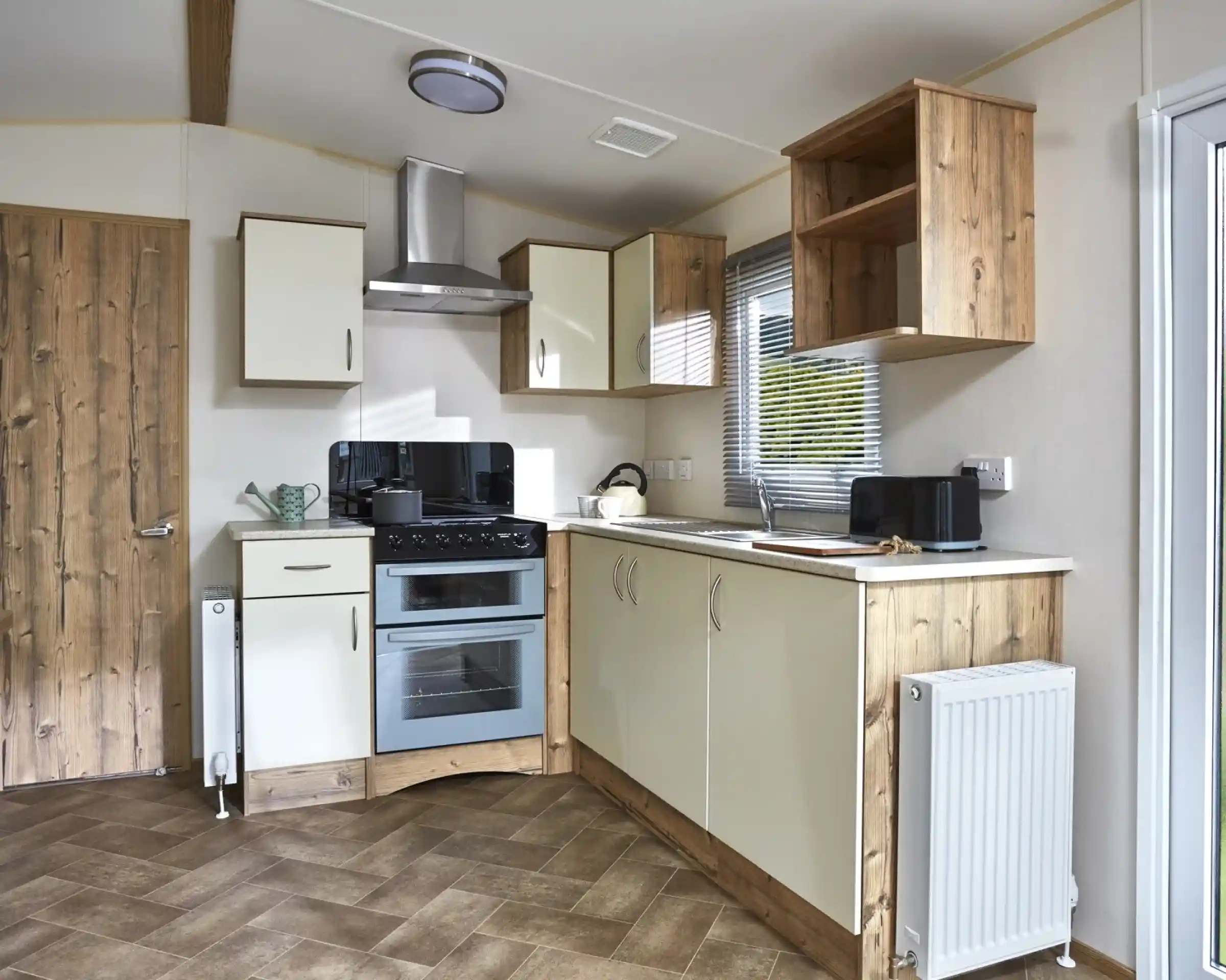 A modern caravan kitchen with cream cabinets, a double oven, and wooden accents.