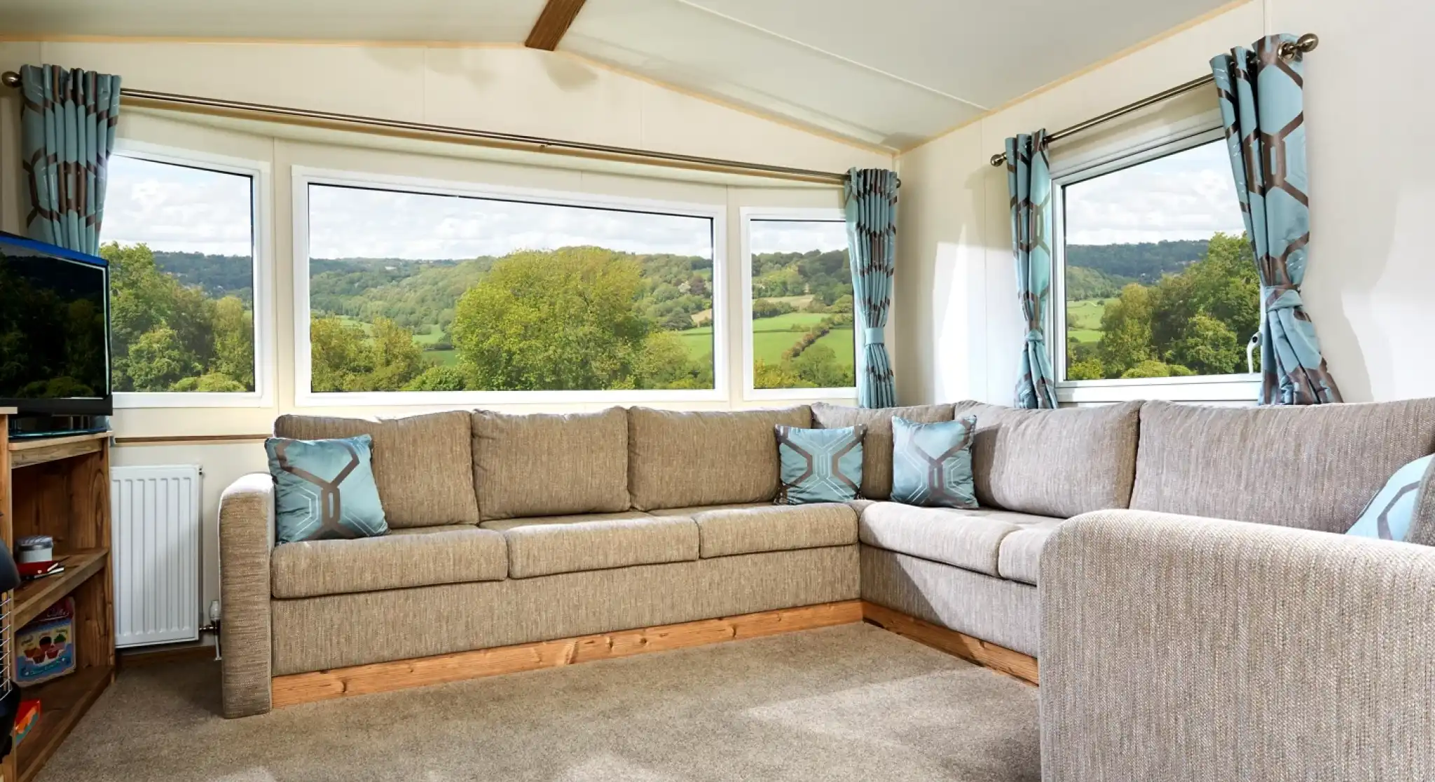 Corner sectional sofa in a living room with large bay windows overlooking a green, hilly landscape.