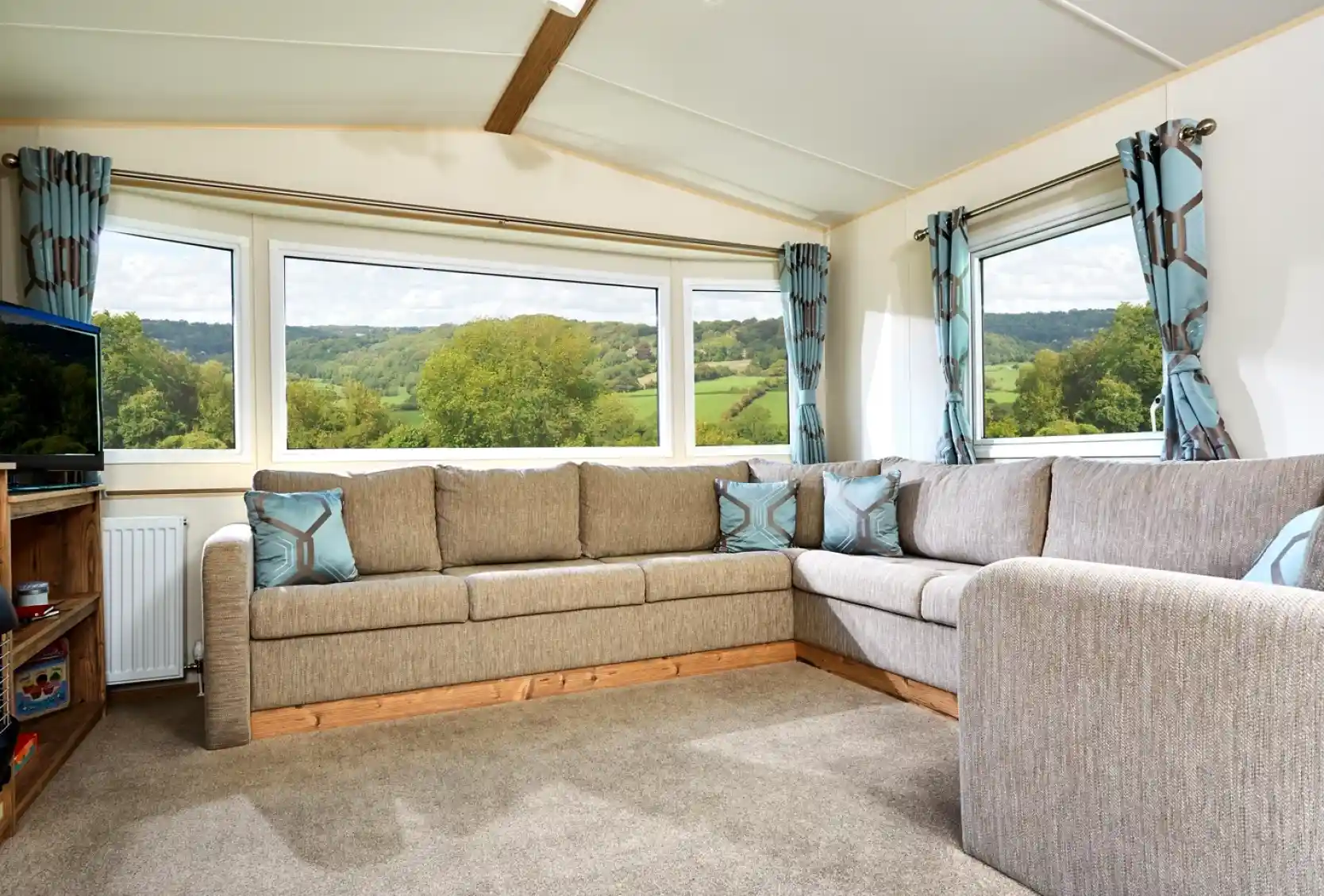 Corner sectional sofa in a living room with large bay windows overlooking a green, hilly landscape.