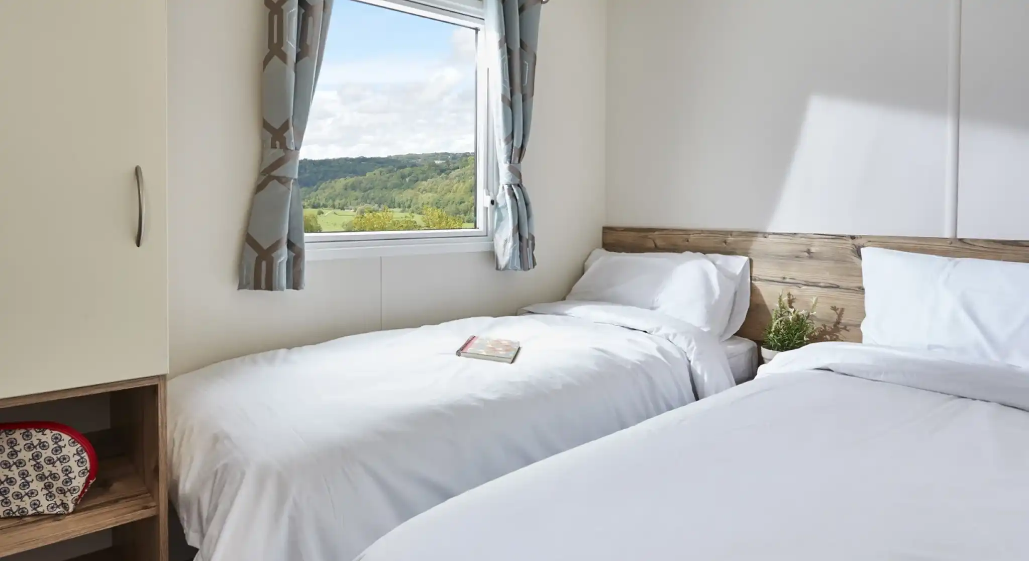 Bedroom with two twin beds, white bedding, patterned curtains, and a window overlooking a green landscape.