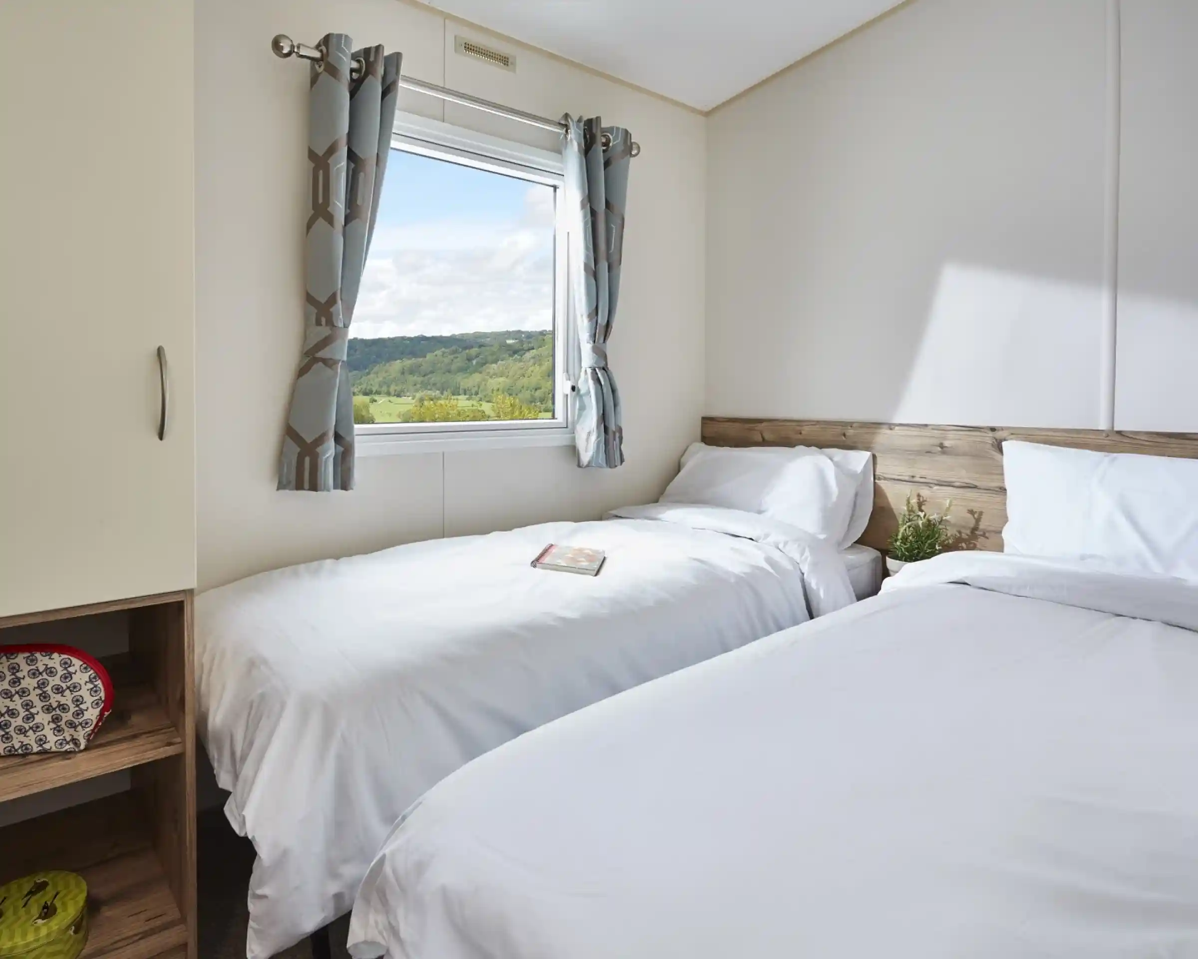 Bedroom with two twin beds, white bedding, patterned curtains, and a window overlooking a green landscape.